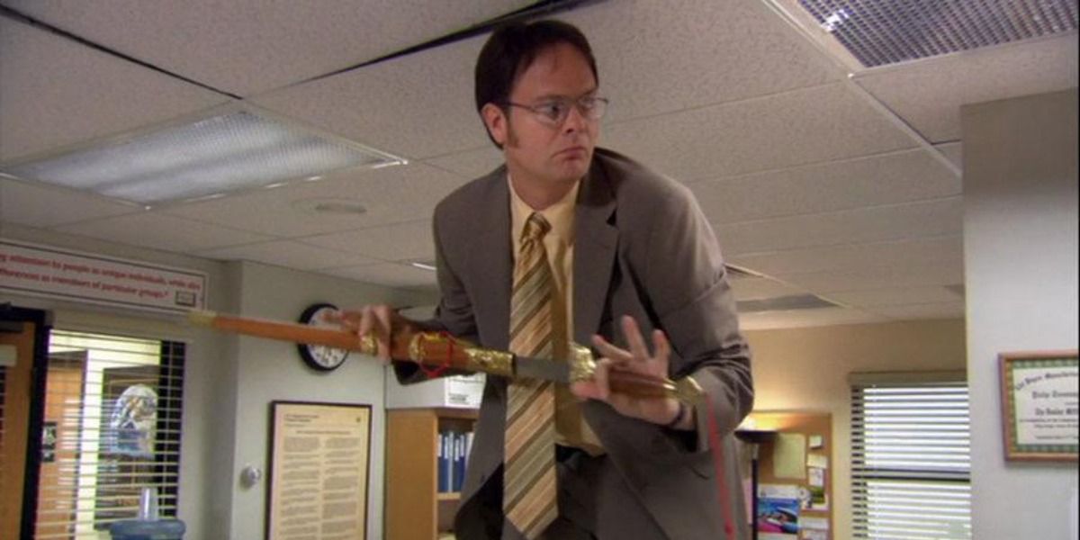 Dwight Schrute from The Office standing on his desk holding a samurai sword